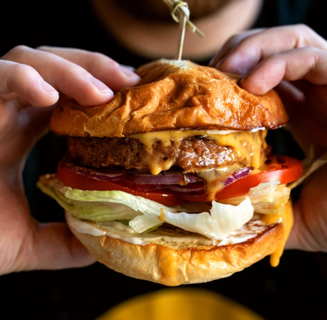 Homme tenant dans ses mains un burger généreux illustrant le travail de Ty'Djo, foodtruck de burgers dans les Côtes-d'Armor.
