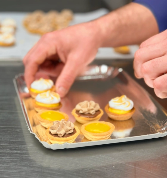 Jonathan, traiteur pâtissier événementiel, disposant sur un plateau des mini tartelettes meringuées préparées dans son atelier dans les Côtes-d'Armor.